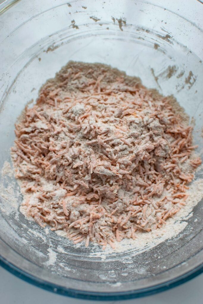 Shredded carrots tossed with flour in a glass bowl.