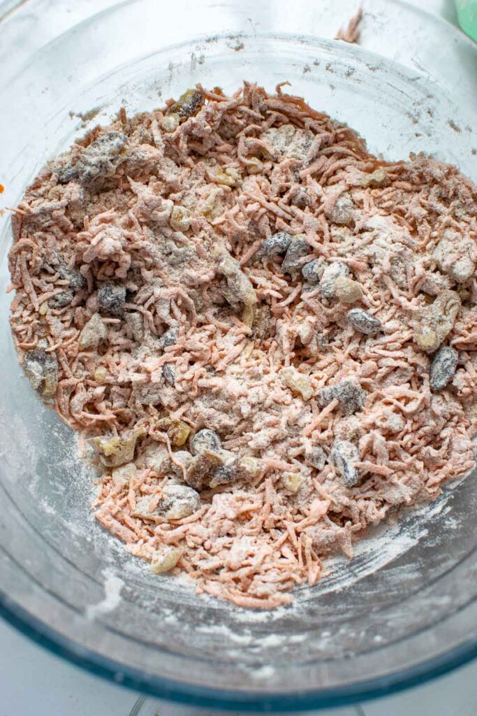 Walnuts tossed with flour and crated carrots in a glass bowl to make carrot cupcakes.