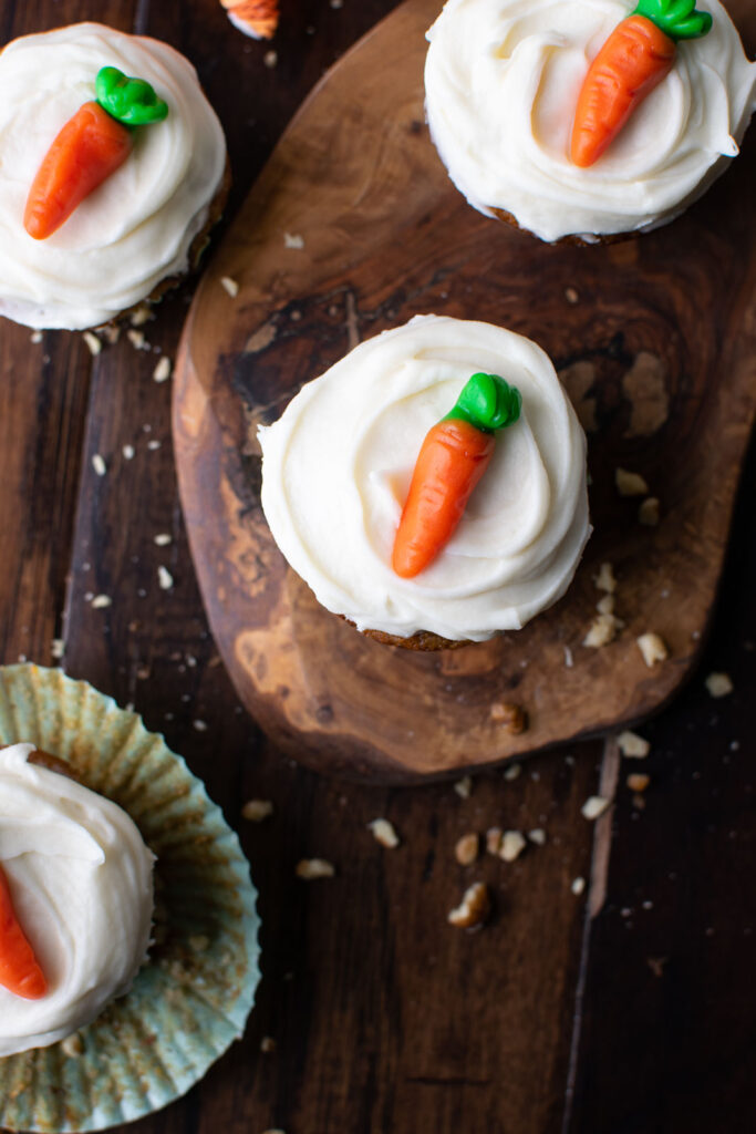 An overhead view of carrot cupcakes topped with cream cheese frosting a gummy candy carrot on top of each.