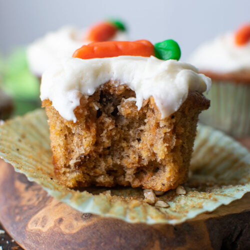 A frosted carrot cupcake with a bite taken out of it.