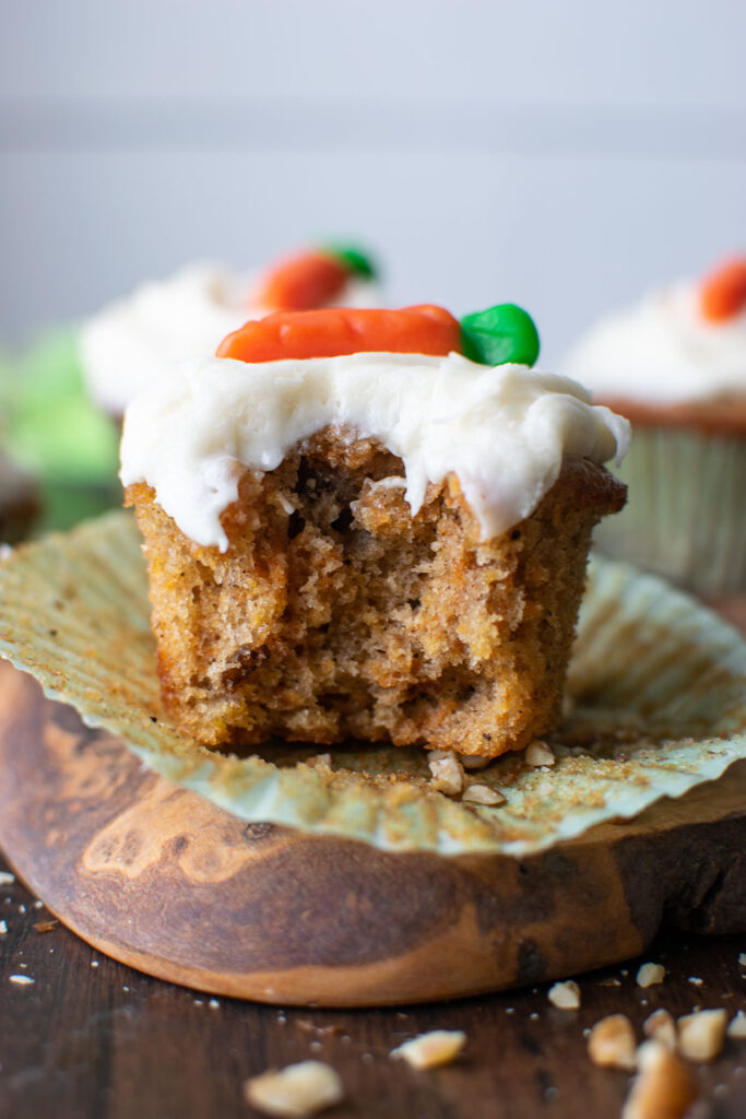 A frosted carrot cupcake with a bite taken out of it.