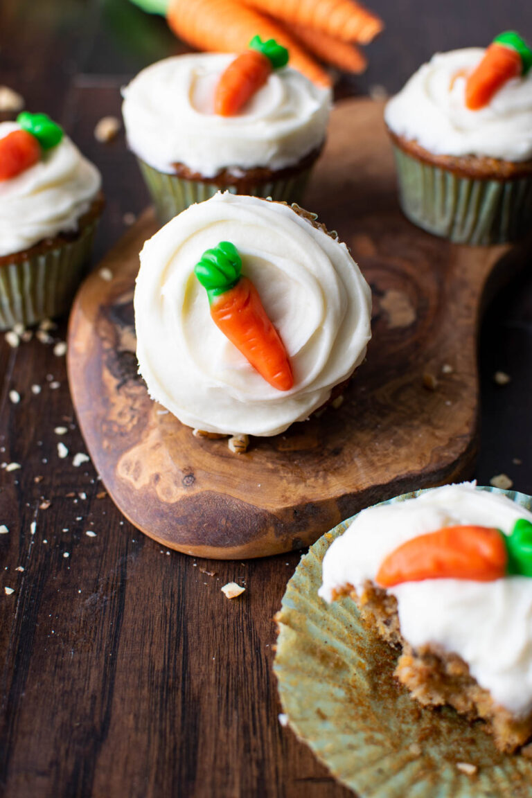 A carrot cupcake with cream cheese frosting and a candy carrot on top.