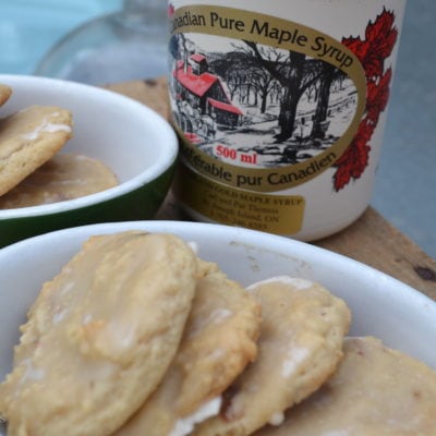 A plate of maple bacon cookies with a jug of maple syrup in the background.