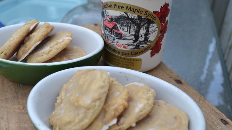 A plate of maple bacon cookies with a jug of maple syrup in the background.