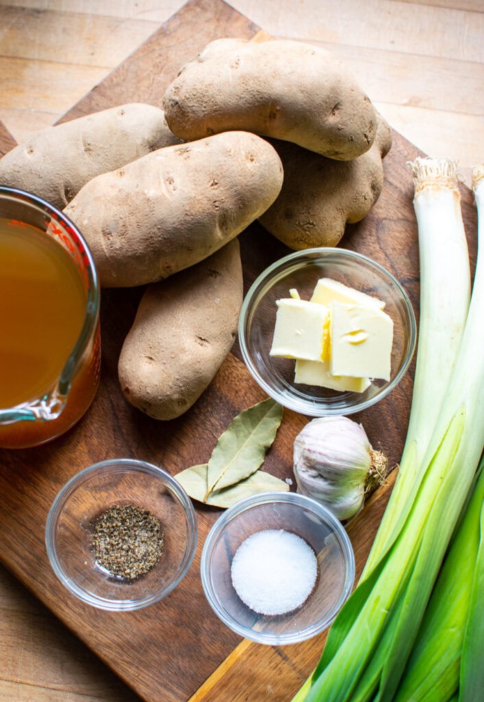 Ingredients to make potato leek soup on a wooden cutting board.