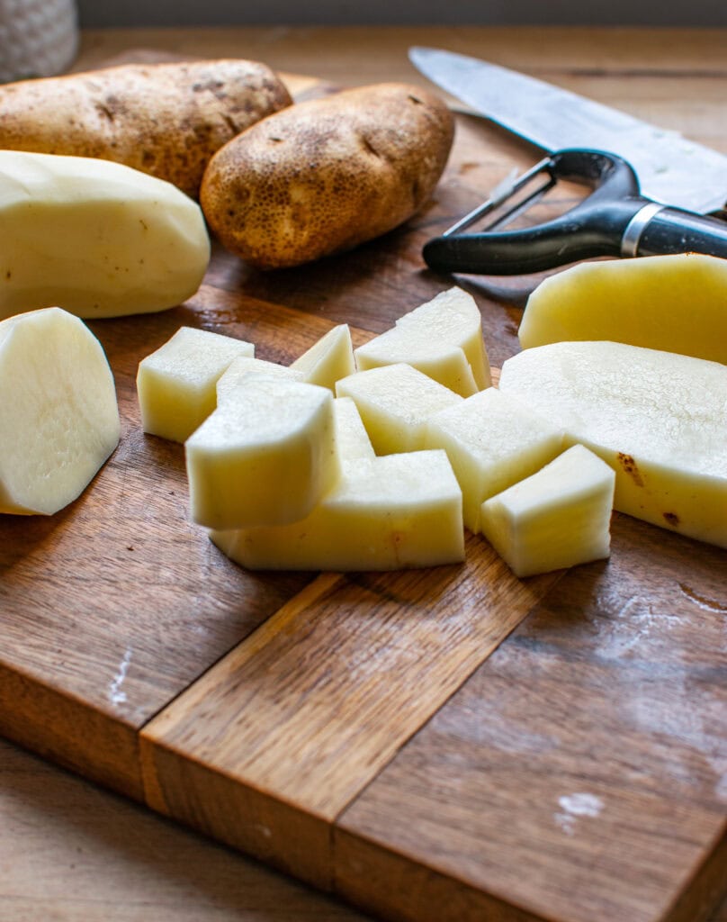 Potatoes on a cutting board, some are peeled and some are chopped.