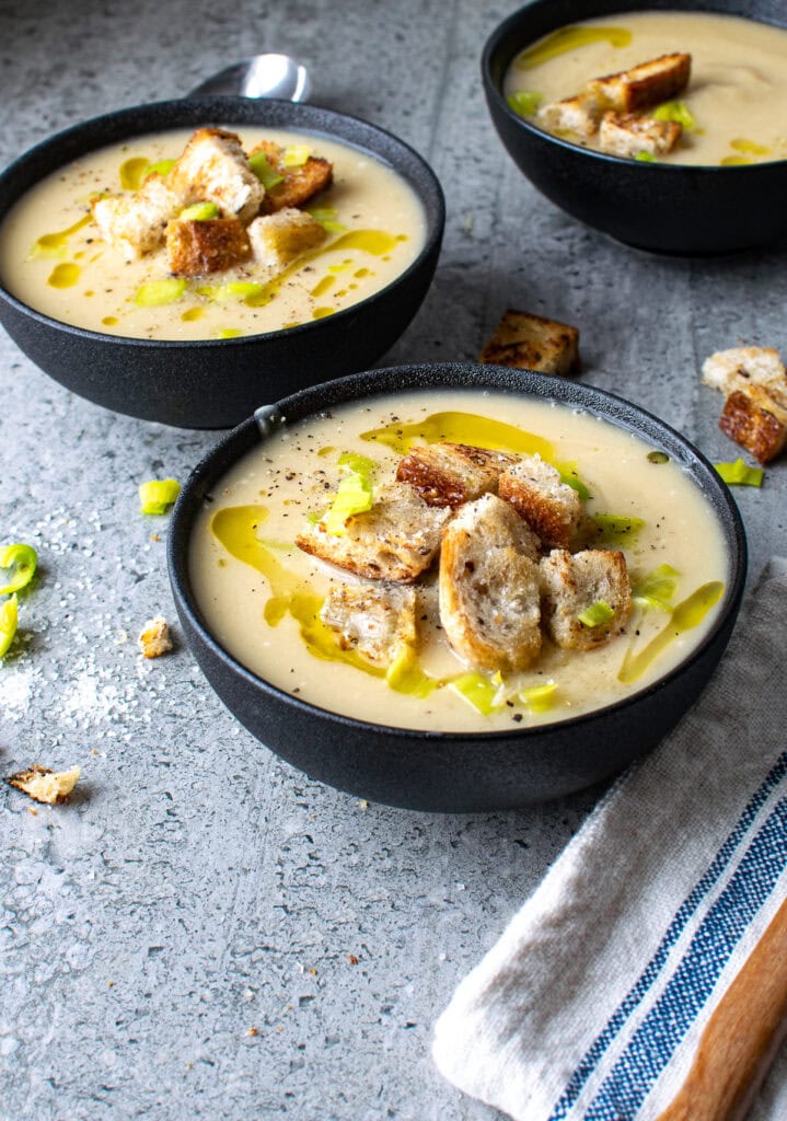 2 bowls of potato leek soup without cream served in a black bowl and topped with croutons and olive oil.