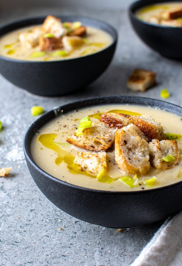 A close up of a bowl of potato and leek soup made without cream in a black bowl and topped with croutons.