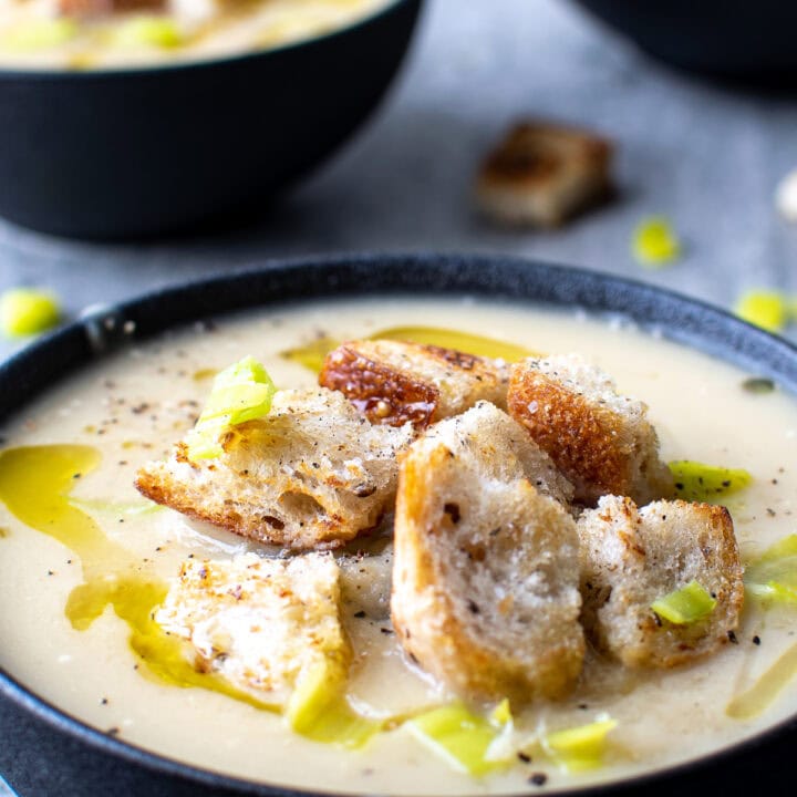 A close up of a bowl of potato leek soup in a black bowl and topped with croutons.