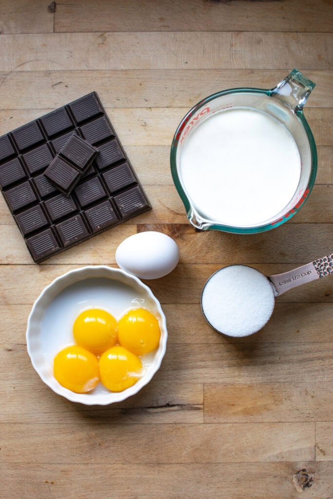 Ingredients to make dark chocolate mousse, including egg, egg yolks, dark chocolate, cream and sugar.