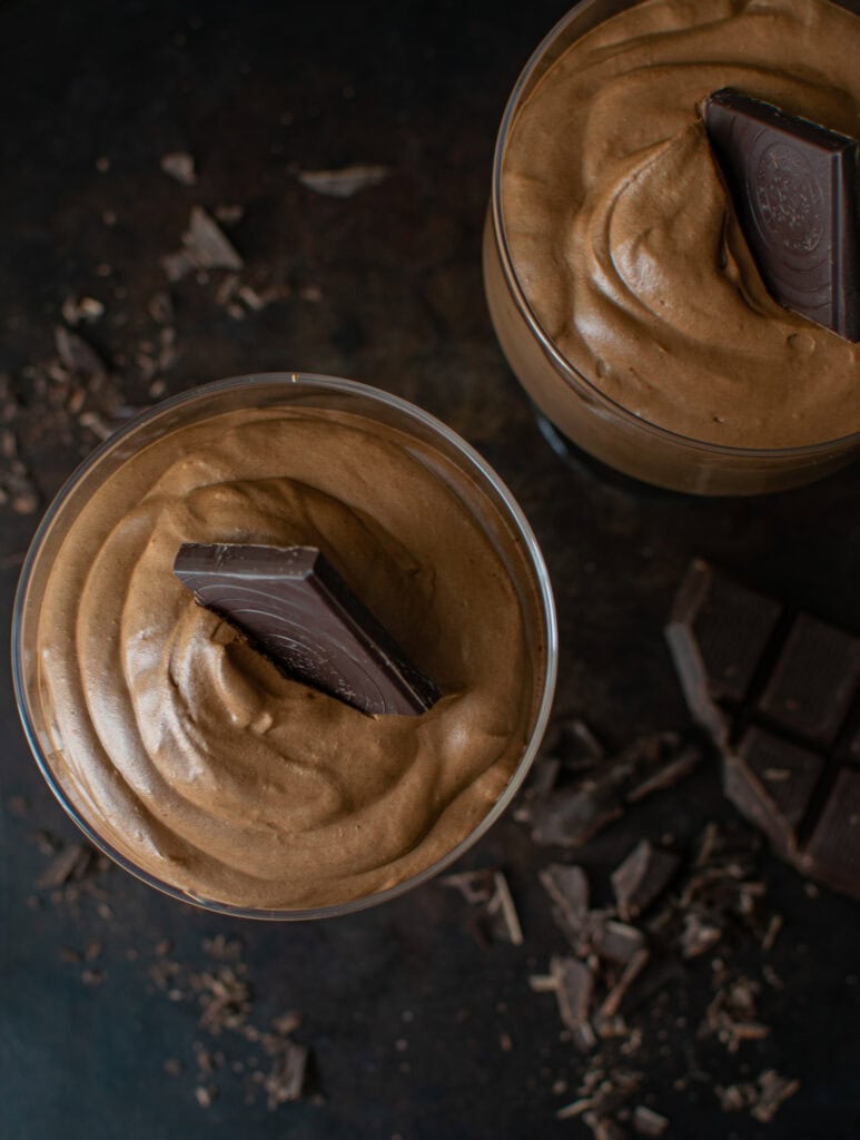 An overhead view of 2 dessert cups of chocolate mousse topped with a square of chocolate.