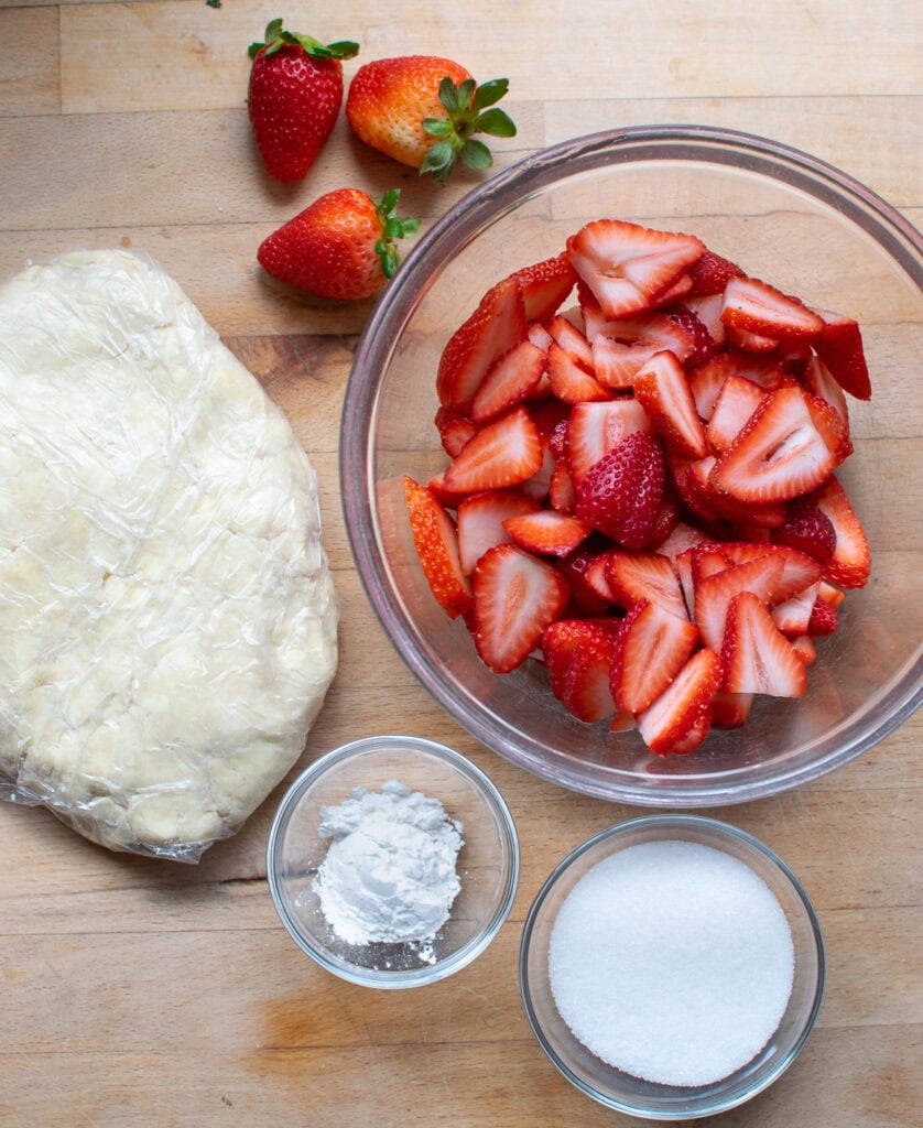 Ingredients to make a strawberry galette including strawberries, sugar, pie crust and cornstarch.