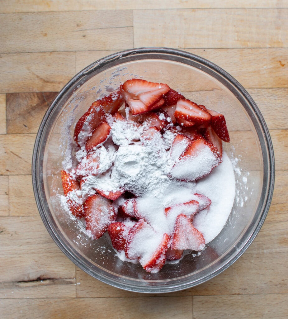 Sliced fresh strawberries in a glass bowl topped with cornstarch and sugar.