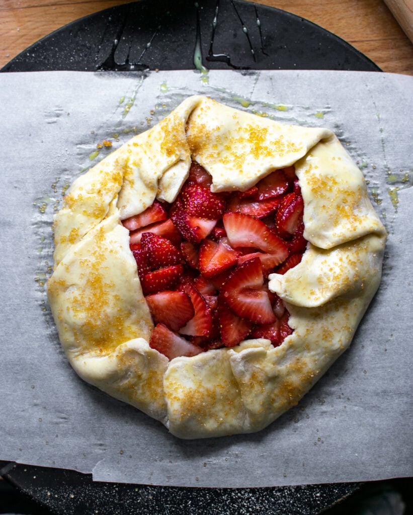 An unbaked galette that has been brushed with an egg wash and sprinkled with course sugar.