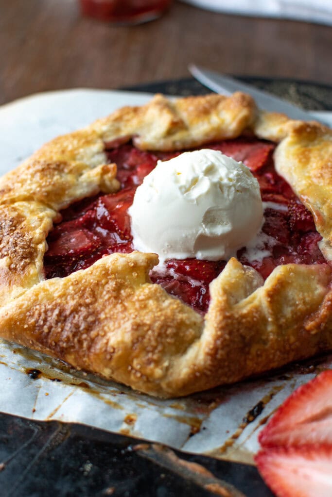 A sweet fruit galette made with strawberries is topped with a scoop of ice cream.