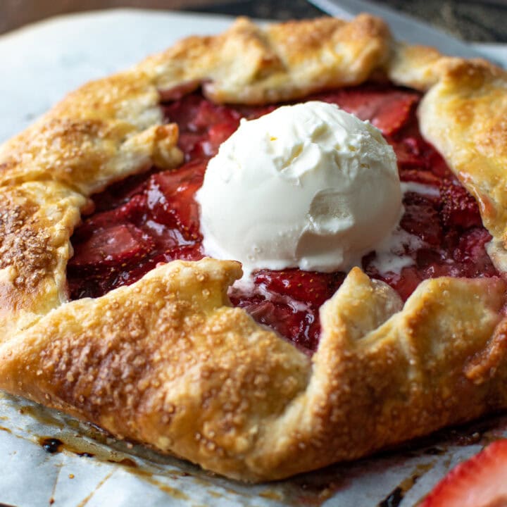 A sweet fruit galette made with strawberries is topped with a scoop of ice cream.