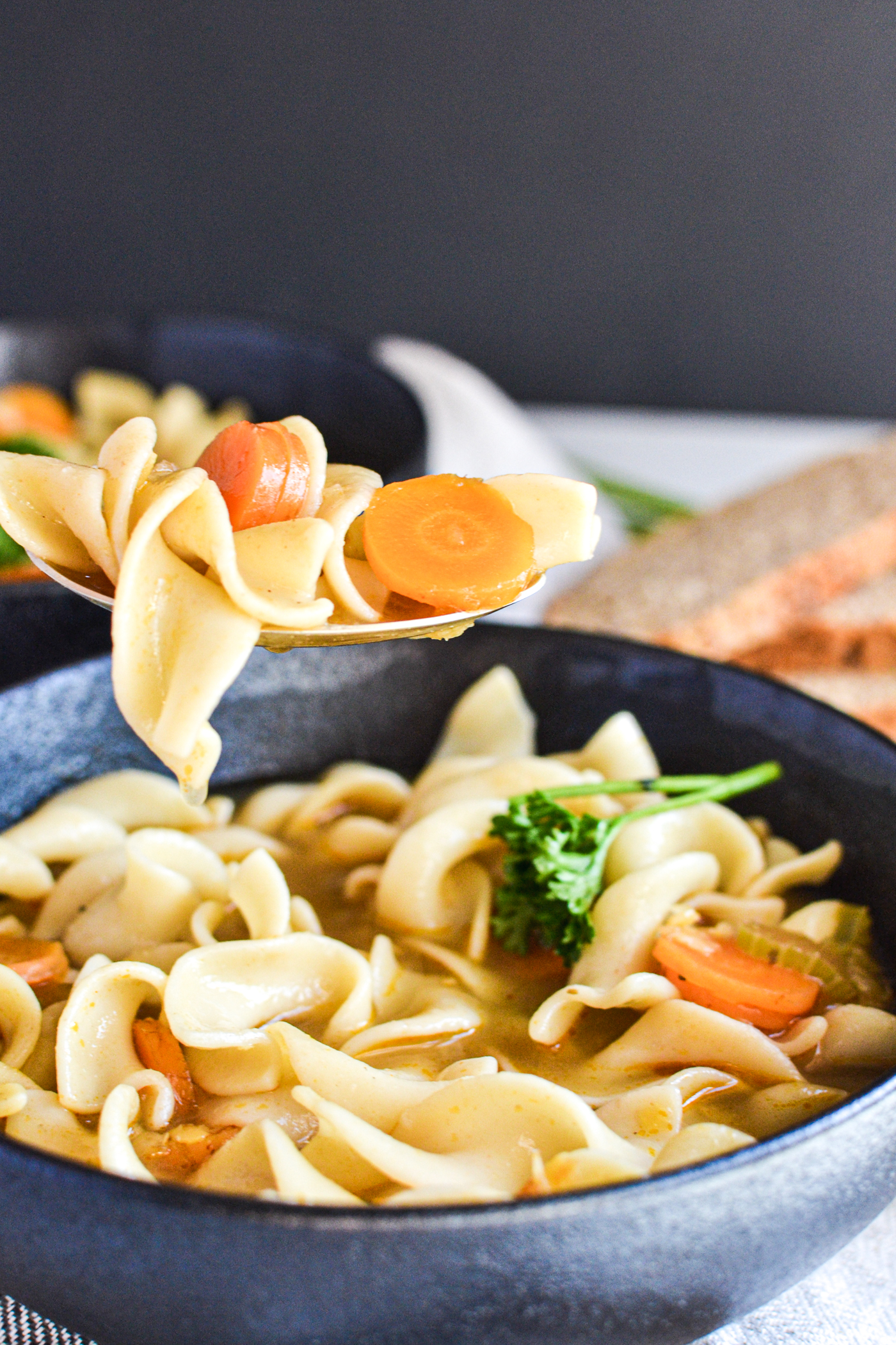 A fork full of noodle soup with broth dripping into the bowl