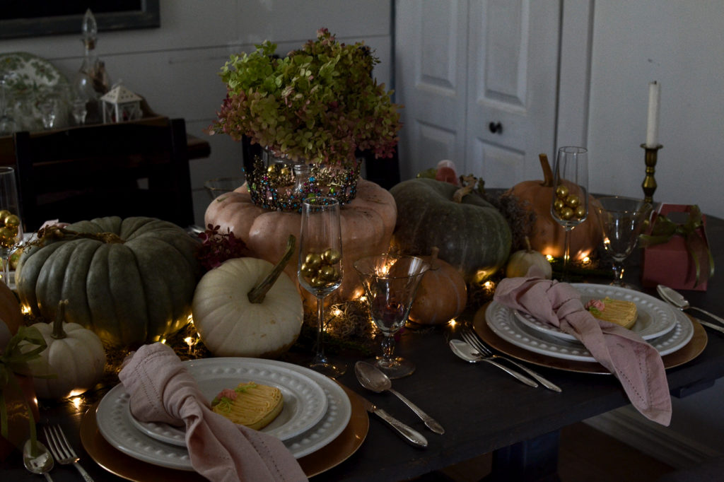 A pumpkin themed Halloween table with twinkle lights surrounding pumpkins down the middle of the table
