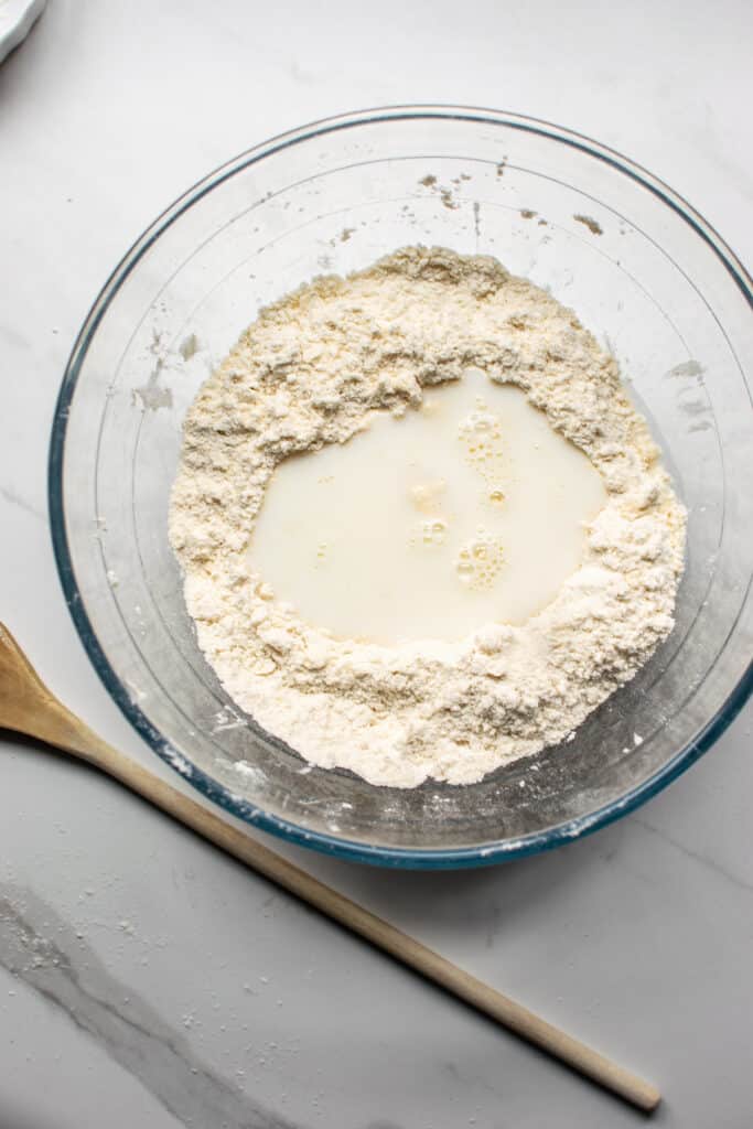 Milk poured into a well made in the dry ingredients for cinnamon rolls with no yeast