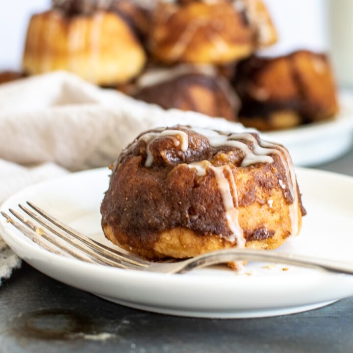 Cinnamon rolls without egg or yeast with a simple glaze on a white plate and silver fork.