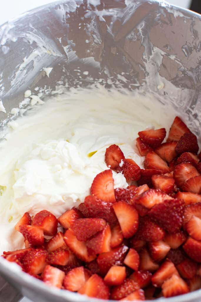 cut strawberries added to a mixing bowl with whipped cream