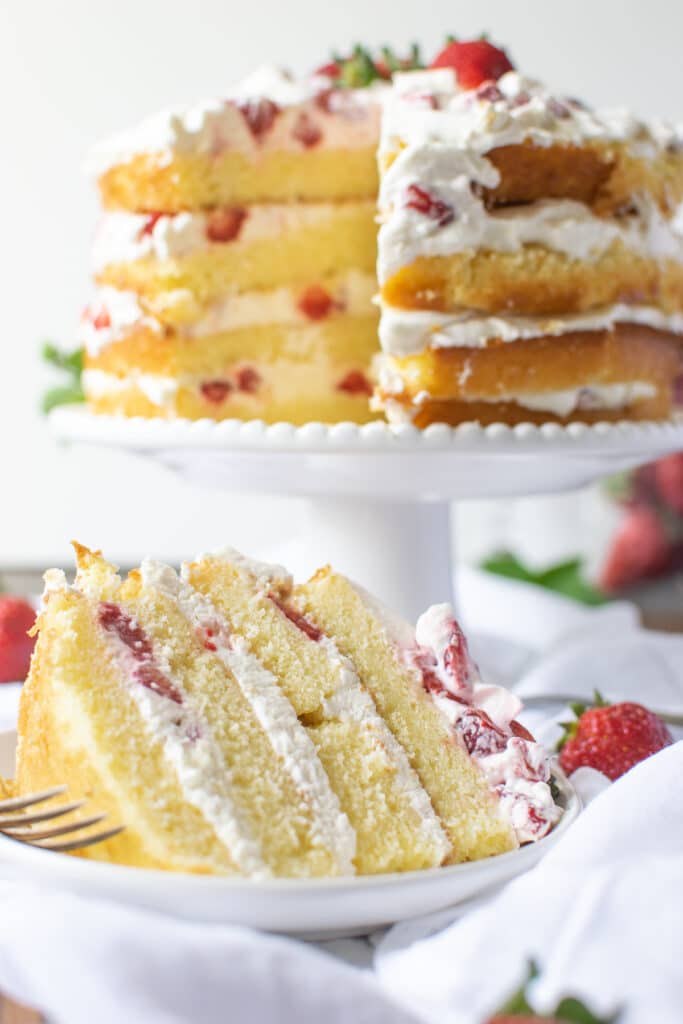 Strawberry and whipped cream layer cake with a slice cut out of it and placed on a plate.