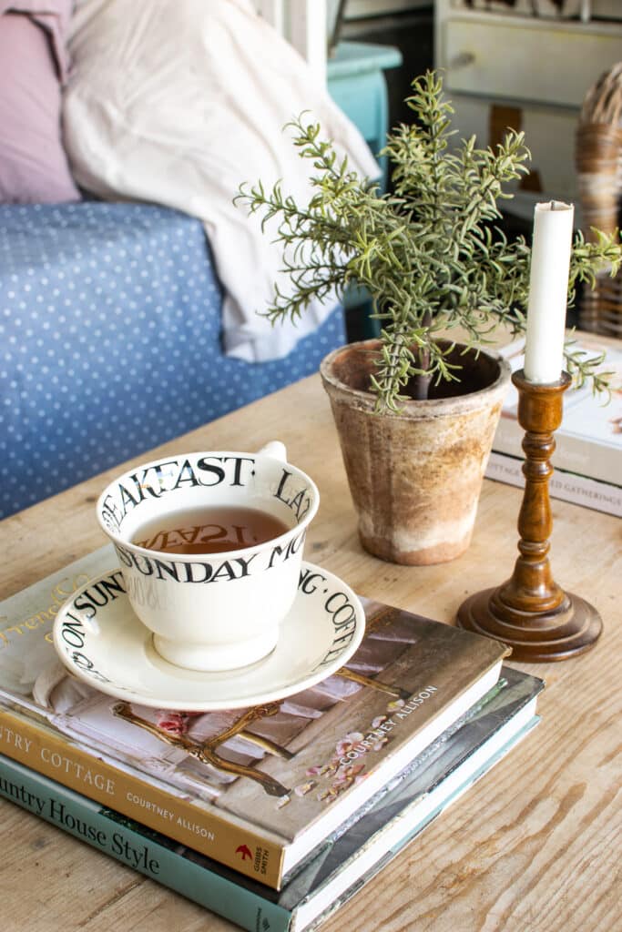 A coffee table with stacks of books, a green plant, wooden candle stick and a tea cup and saucer.