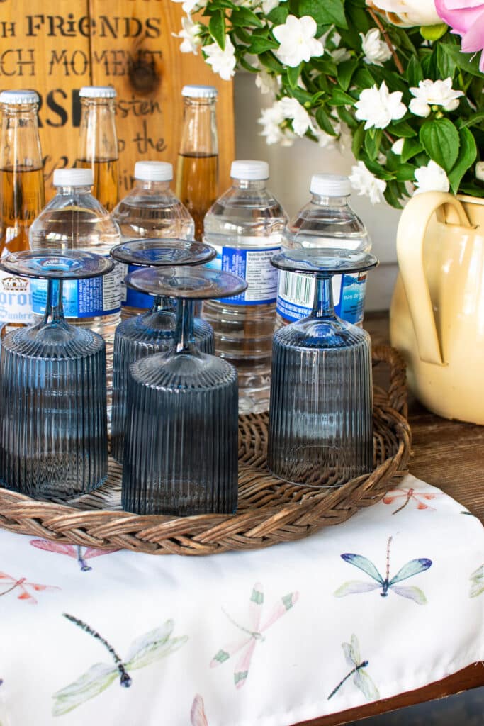 Blue drinking glasses, bottled water and flowers on a side table.