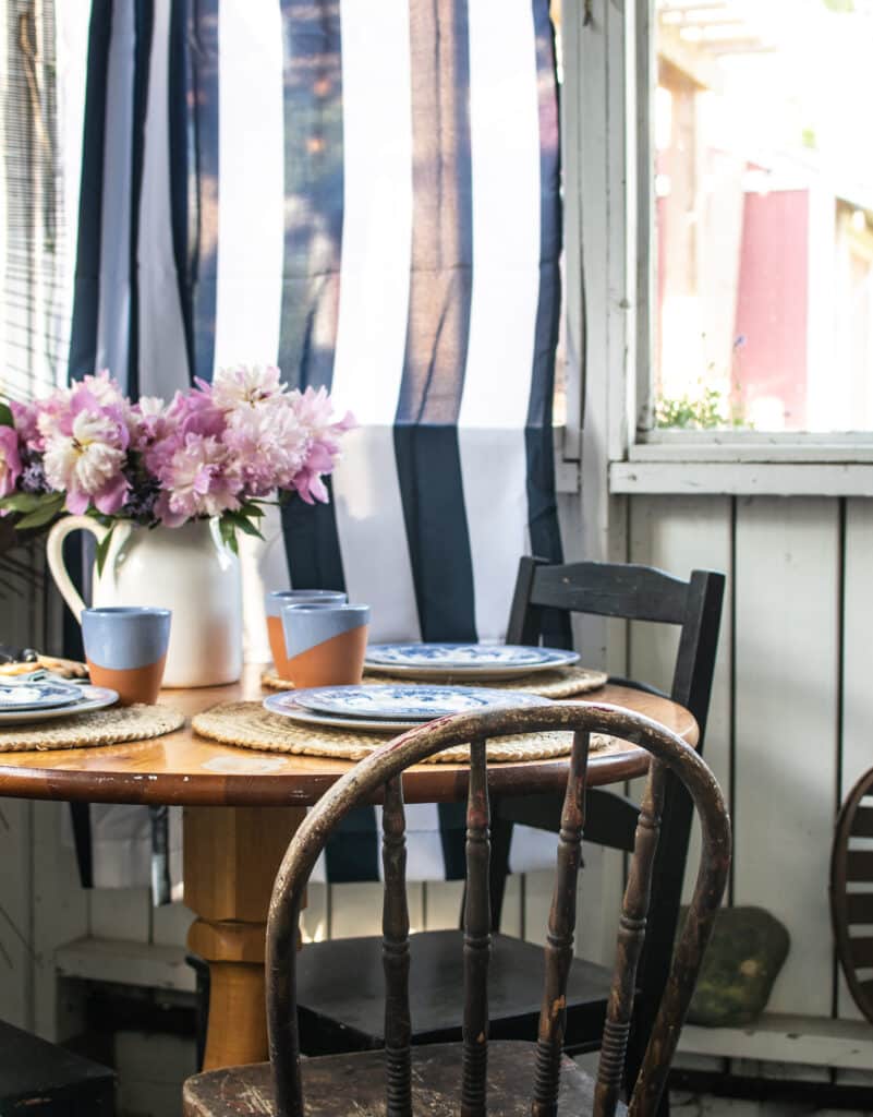 Round table with a vase of pink peonies set with blue dishes.