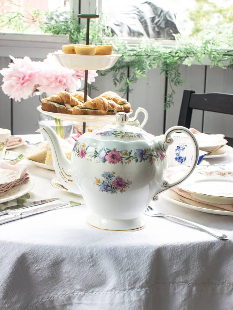 A floral pattern tea pot on a table set for afternoon tea