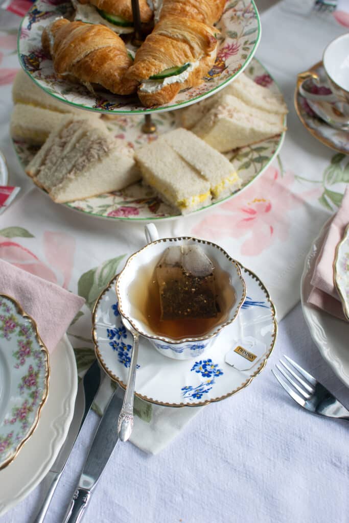 An overhead view of a tea cup filled with tea beside a plate of sandwiches.