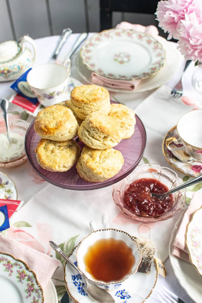 An plate of English scones with a bowl of strawberry jam and a bowl of clotted cream.
