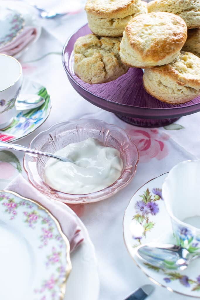 A bowl of clotted cream beside a plate of scones.