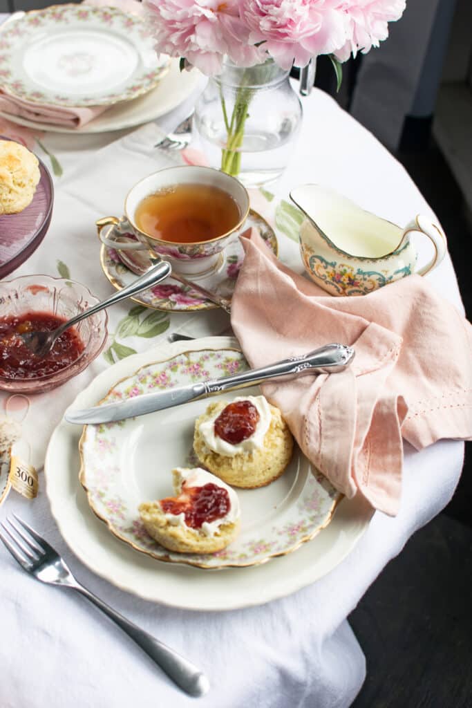 A plate with a scone spread with cream and jam beside a cup of tea