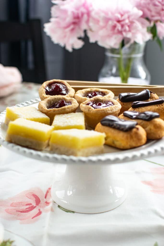 A plate of desserts including mini eclairs, lemon bars and raspberry tarts.