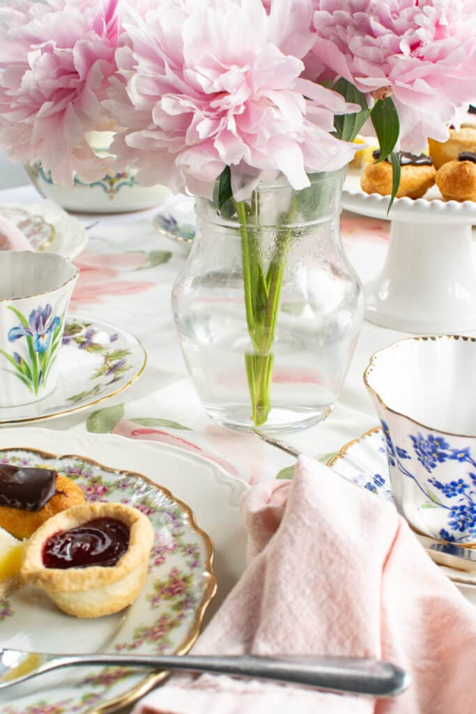 A table set for afternoon tea with pink peonies and a plate of tarts and pastries