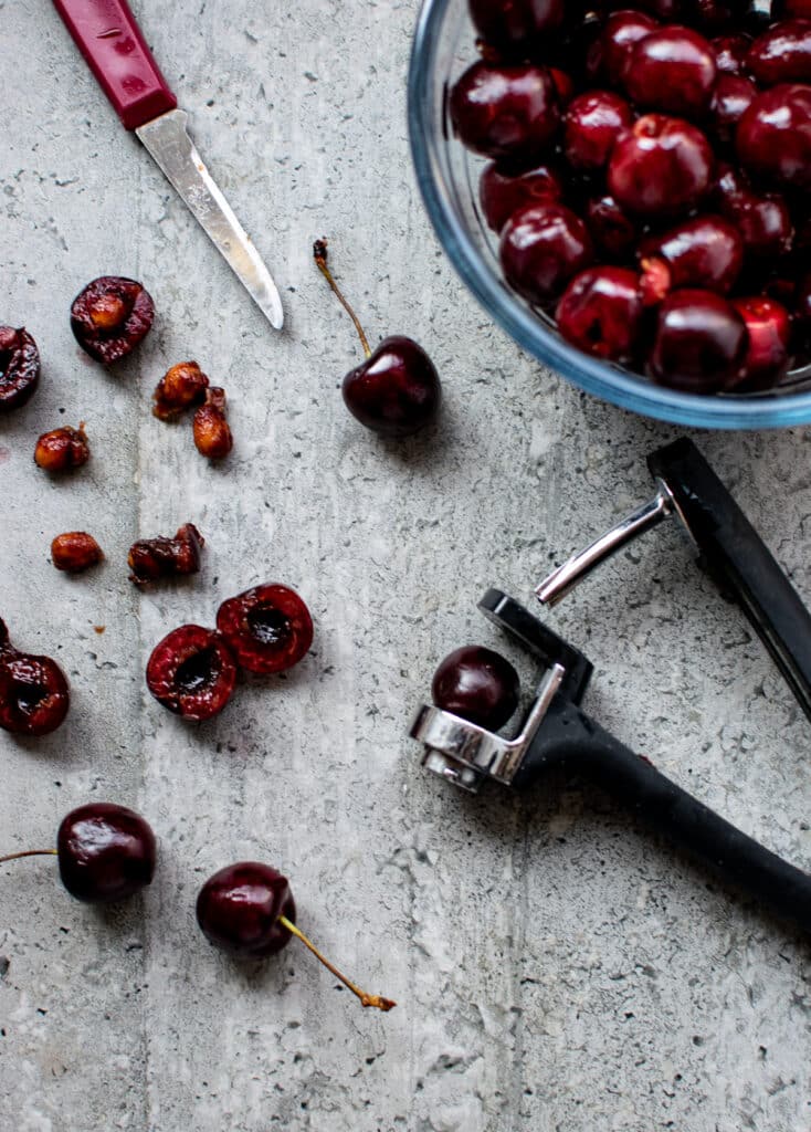 An overhead view of fresh cherries being pitted and slice in half