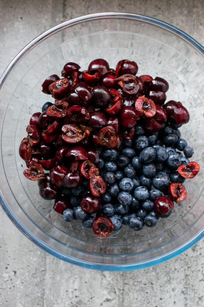 A bowl of fresh blueberries and pitted cherries cut in half.