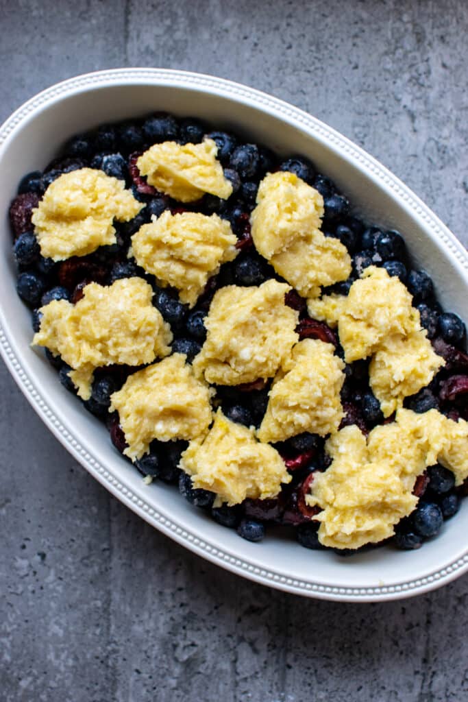 Fruit cobbler topping added to the top of fruit in an oval ceramic baking dish.