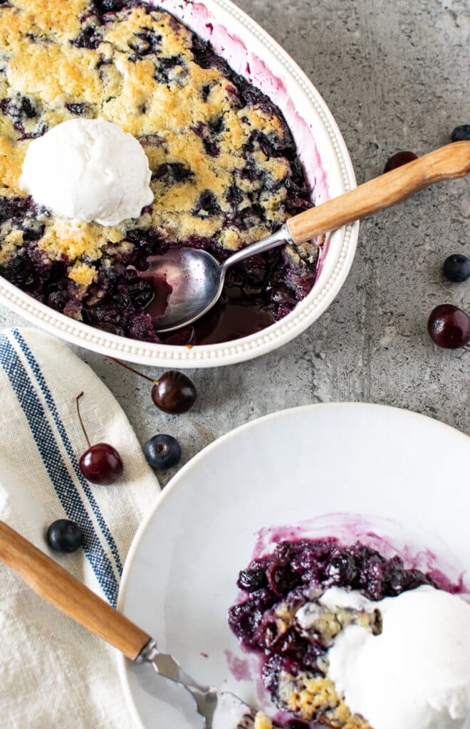 Overhead view of a blueberry cherry cobbler in a white scoop of ice cream on top.