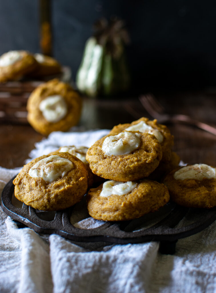 A plate of pumpkin cream cheese thumbprint cookies piled on a pumpkin shaped trivet.