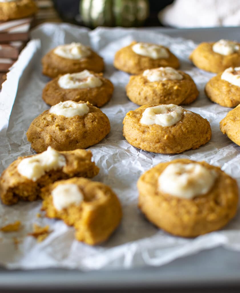 A pan of freshly baked pumpkin cream cheese thumbprint cookies on a baking sheet lined with parchment paper.