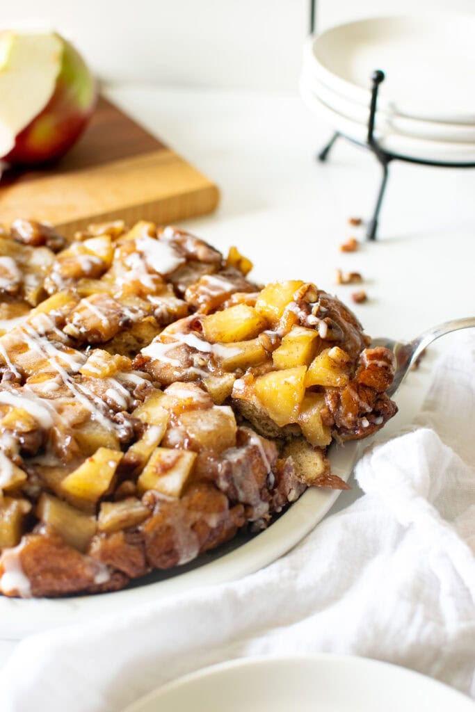 Upside down apple cinnamon roll cake on a white cake plate set on a marble counter.