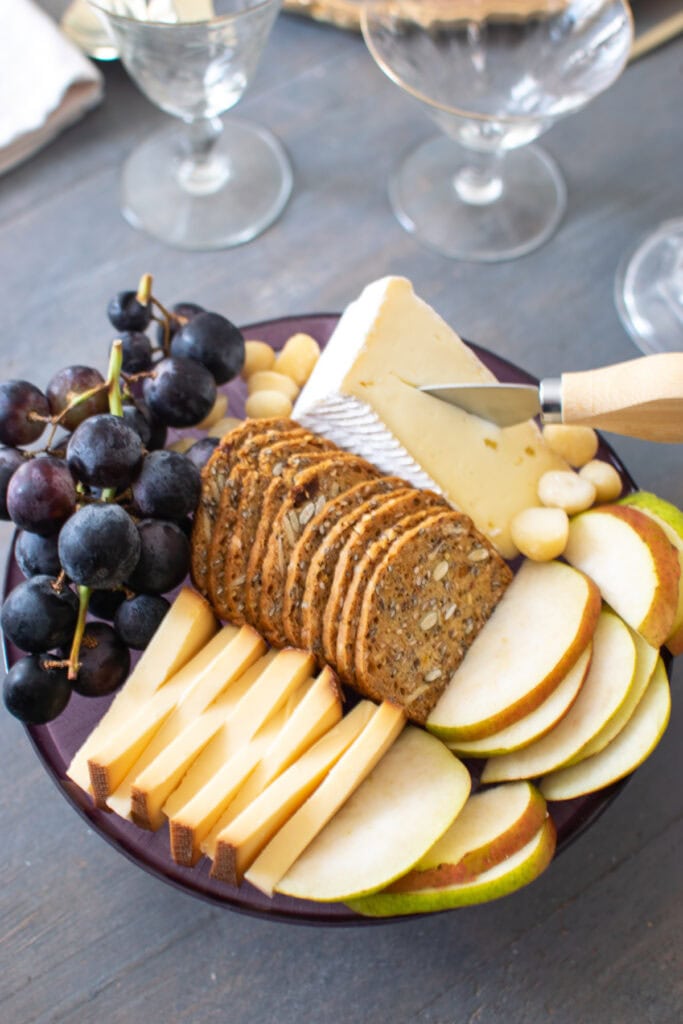 A small cheese and fruit platter with crackers, smoked Gouda cheese, brie, sliced pears and purple grapes.