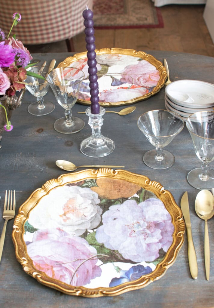 Two place settings with floral charger plates, gold flatware and gold rimmed glasses.