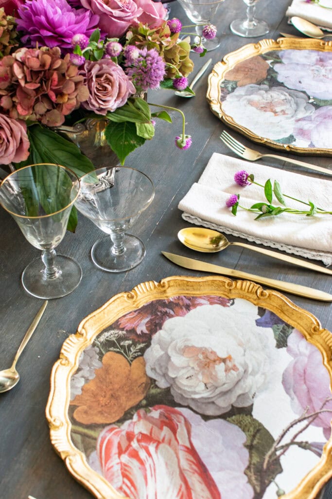 An overhead view of a table set for autumn, with floral patterned charger plates and a purple floral centrepiece.