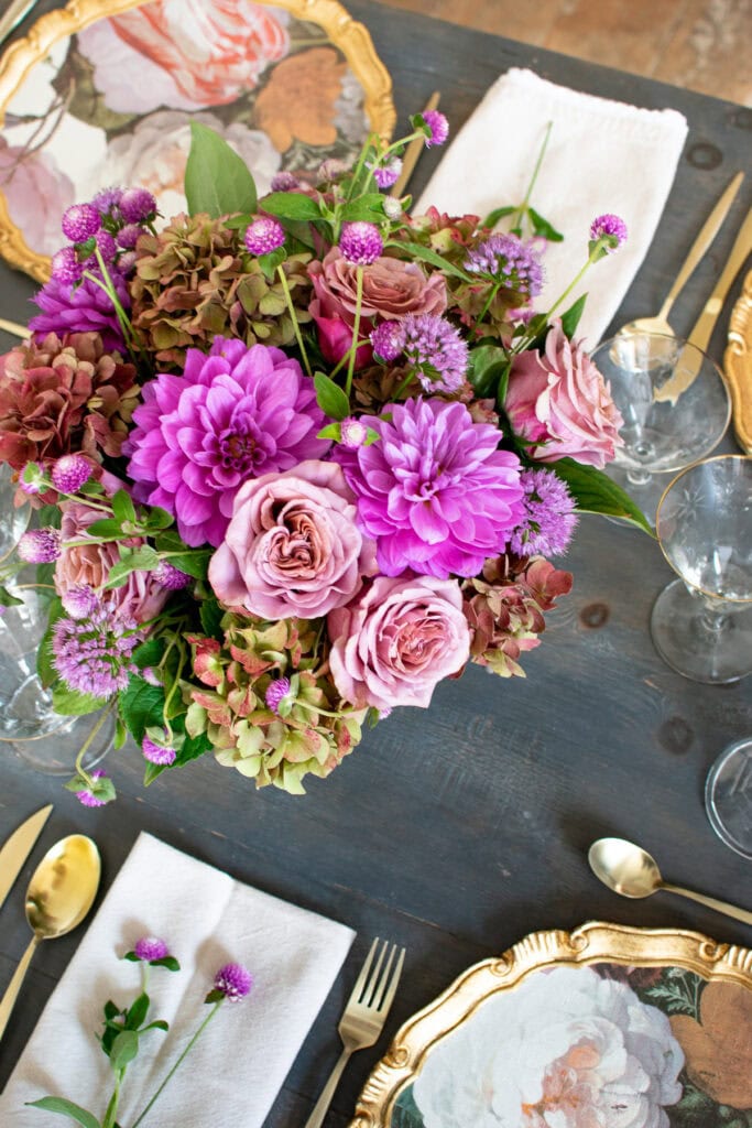 Overhead view of a dinner table centrepiece with purple dahlias, mauve roses and mauve/green hydrangea.