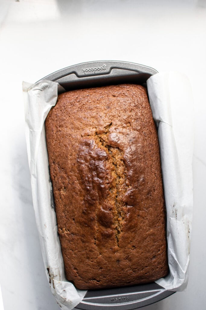 A freshly baked loaf of pumpkin bread still in the parchment lined loaf pan.