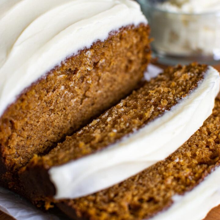 Pumpkin bread with cream cheese frosting with two slices cut and stacked in front of the loaf.