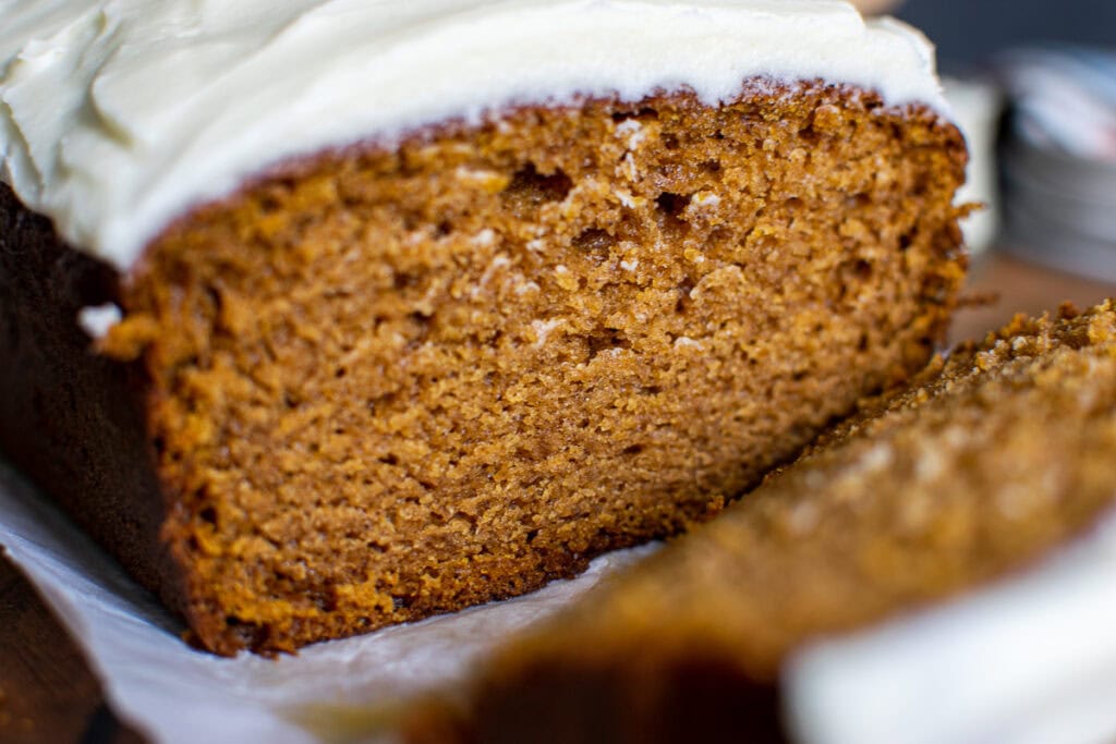 Close up of a slice of frosted pumpkin bread to show fine, moist crumb the recipe produces.